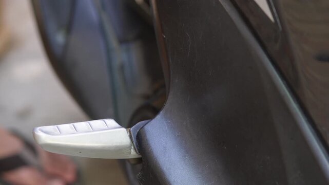 A person's hand opening the motorcycle footstep. Does not show the face.