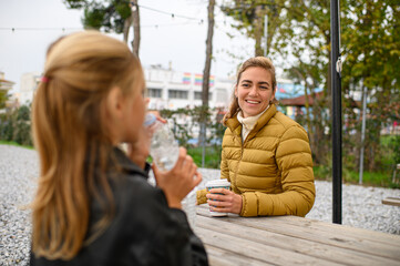 Mother and daughter enjoying coffee at an outdoor café, sitting together at a street table, sharing a warm moment in a relaxed urban atmosphere.