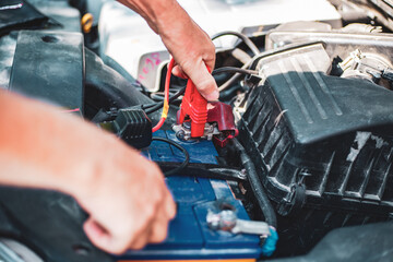 Under the hood of the car, the mechanic connects the clamp of the car jump starter to the terminal of the dead car battery