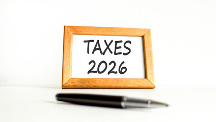 Taxes 2026 new year symbol. Concept words Taxes 2026 on beautiful wooden picture frame. Beautiful white paper background. Beautiful black pen. Business and taxes 2026 new year concept. Copy space.