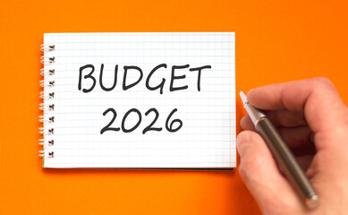 Budget 2026 symbol. Concept words Budget 2026 on beautiful white note. Beautiful orange paper background. Businessman's hand with pen. Business and budget 2026 concept. Copy space.