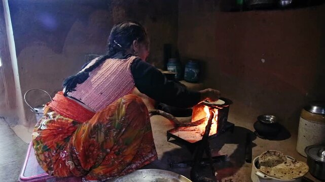 An Indian village woman cooks chapati or fulka on a traditional iron chulha using firewood collected from the nearby Uttarakhand jungle, reflecting rural lifestyle, simple cooking, and daily Himalayan