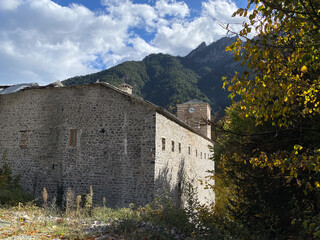 Medieval stone building in mountain landscape with blue sky and autumn foliage