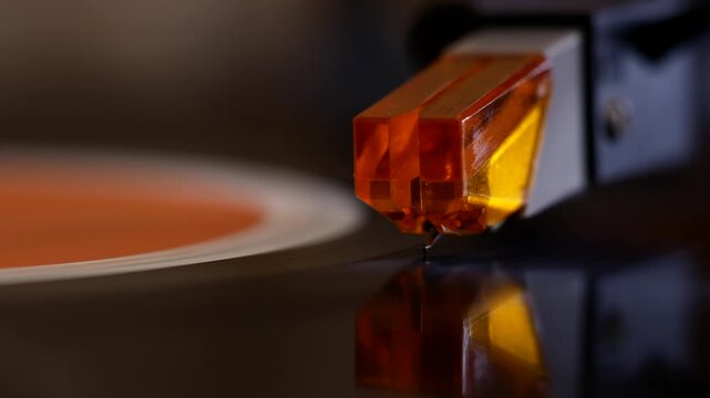 Close-up of a vintage turntable arm lifting the needle from the run-out groove as the spinning vinyl record slows down and halts.