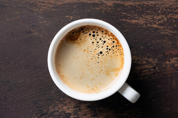 Fragrant cup of black coffee with beautiful coffee foam (crema) in white porcelain cup on old wooden table background
