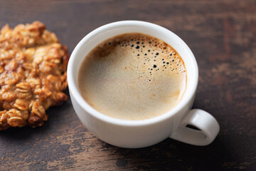 Cup of black coffee and oatmeal cookie on wooden table background. Coffee break closeup view
