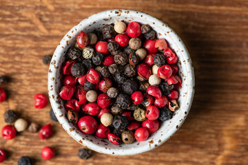 Black, red and white peppercorns in white ceramic bowl, top view. Closeup view of spices for cooking
