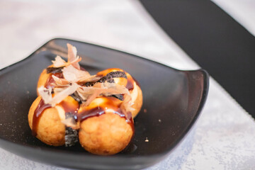 Octopus takoyaki, fried dough balls filled with octopus on a black plate, popular Japanese street food, soft focus