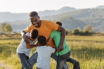 Smiling dad wrestling and playing with his kids outdoors on a sunny day, enjoying family fun in nature. Father-son bonding concept.