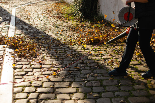 Outdoor worker using a a leaf blower to clear fall leaves from an urban cobbled path, performing autumn maintenance chores