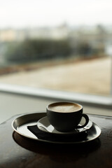 Warm coffee cup on a metal tray next to a window, providing a moment of tranquility with a soft blurred city background
