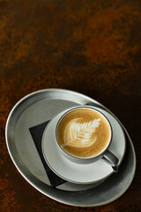 Espresso coffee drink with detailed latte art on foam, serving on a metal tray with a dark background