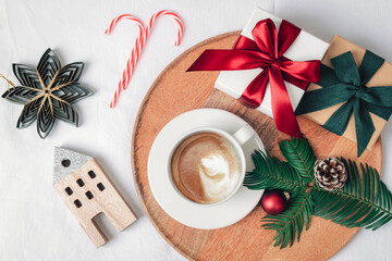 A cup of coffee on a wooden tray surrounded by bright ornaments, gift boxes, ribbons, pine cone and evergreen branch. Christmas holiday concept. Top view, flat lay