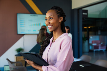 Smiling black young businesswoman with tablet in office with colleagues in background