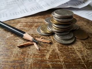Broken Pencil Tip Next to a Stack of Coins on Wooden Surface