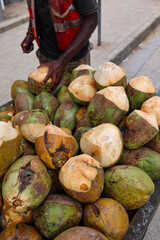 Fresh young coconuts displayed on a street market stall, with a vendor holding a peeled coconut. Tropical produce, natural textures and vibrant green and brown colors create an authentic Zanzibar 