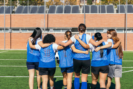 Female football players forming a huddle, showing teamwork, friendship and unity on a green grass field - Powered by Adobe