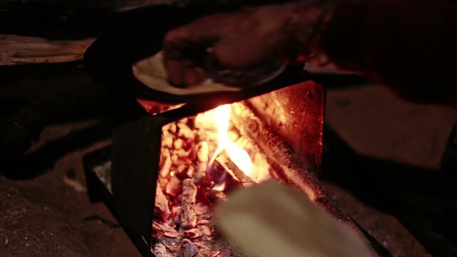 An Indian village woman cooks chapati or fulka on a traditional iron chulha using firewood collected from the nearby Uttarakhand jungle, reflecting rural lifestyle, simple cooking, and daily Himalayan