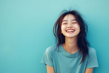 Fototapeta premium Happy young Asian woman closing her eyes and openly laughing, expressing positive emotions and carefree living
