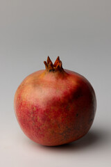 Whole pomegranate photographed frontally on a plain background, showing its vibrant red skin and natural texture in a clean, minimal, food-focused composition.