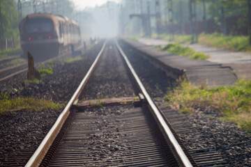 Fototapeta premium Morning view of a train moving along railway tracks, captured with soft mist and natural light at a quiet rural station.