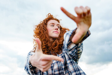 Creative woman making a frame gesture against cloudy sky