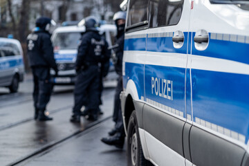 German police car from berlin is in the focus and in the blurry background are several riot police cops standing on the street and waiting for action on a demonstration. © Ben D.