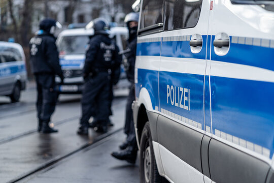 German police car from berlin is in the focus and in the blurry background are several riot police cops standing on the street and waiting for action on a demonstration.
