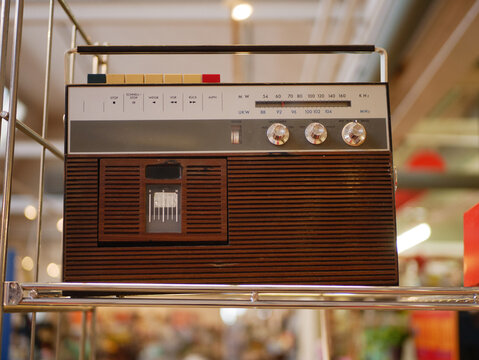 A vintage portable radio cassette player with a wood panel finish and analog controls displayed on a metal shelf. The device represents classic audio technology and retro design. Perfect for