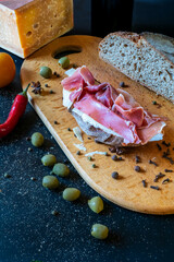 Delicious Italian bruschetta with prosciutto (ham), cheese, and olives on a wooden board. Gourmet appetizer in dark food photography style. Ready to eat