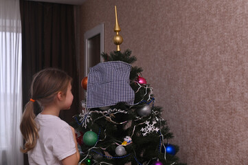 little girl putting finishing touches on Christmas tree, placing star on top. room is filled with holiday cheer. child standing beside Christmas tree, adding final decorations with golden star on top.