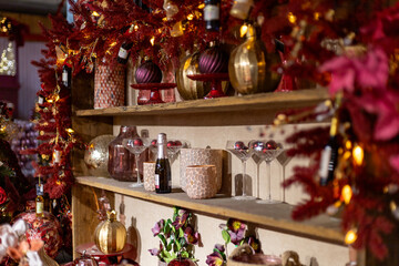 Cozy festive shelf decorated with red and gold ornaments, glassware, lights, and holiday garlands, creating a warm Christmas atmosphere.