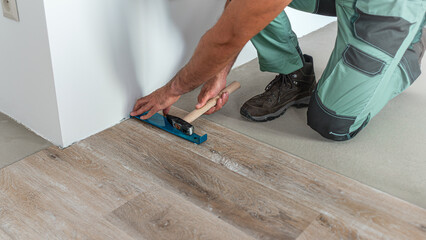 Floating floor work. The worker's hands beat to the sheet metal hook with hammer to lock the floor click system.
