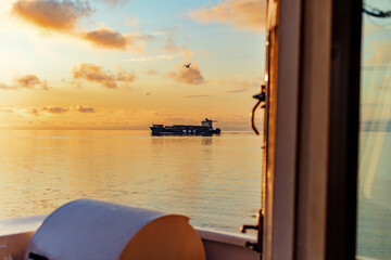 Editorial. 1 July 2025 Baltic Sea. Container ship at sea during a calm sunset, viewed from another vessel. Soft golden light, gentle waves and distant cargo vessel create a peaceful maritime scene.