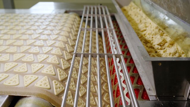 Automated production line forming cheese-shaped crackers from dough, illustrating modern food manufacturing processing