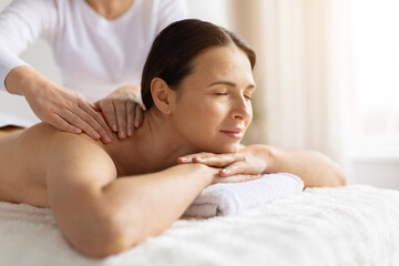 Young female enjoying body massage at spa, eyes closed and resting on towel. Soft lighting and calm atmosphere emphasize beauty, wellness care and a peaceful, soothing lifestyle moment