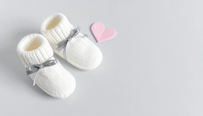 White Knitted Baby Booties with Grey Bows and Pink Heart. Minimalist Newborn Announcement Flat Lay with Copy Space.