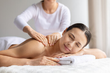 Young woman receiving gentle upper back massage at spa. Soft hands, warm light and tranquil atmosphere highlight beauty care, wellness, relaxation and a soothing self-care lifestyle experience