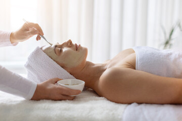 Beautician applying face clay mask to young beautiful woman at spa. Female client enjoying beauty care, skincare renewal and a tranquil wellness lifestyle experience