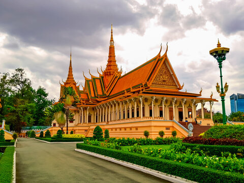 The elegant Throne Hall of the Royal Palace in Phnom Penh stands majestically with its classic Khmer architecture and ornate golden spires, set against a dramatic cloudy sky and surrounded by gardens. - Powered by Adobe