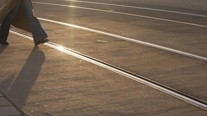 Human crossing a sunlit tram track. Lens flare in image.d