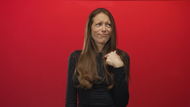 Woman points thumb to self with questioning face in red studio wearing black top; skepticism introspection.