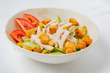 A colorful salad with grilled chicken, cucumbers, and croutons in a bowl