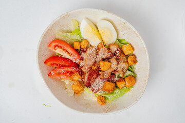A colorful salad features crisp lettuce, sliced tomatoes, hard-boiled eggs, croutons, and bacon
