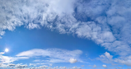 Beautiful blue sky background with cirrus and cumulus clouds. Large and small vapor structures are arranged in a chain, flowing smoothly along the horizon. Wide website banner.