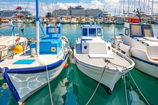 Fishing boats and cruise ships line Manfraki harbor and port at the medieval seaside city of Rhodes, Greece, on the island of Rhodes.