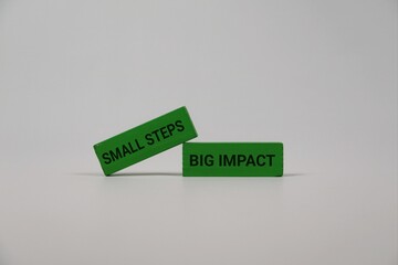 Two green blocks with 'Small Steps' and 'Big Impact' rest on an white backdrop, illustrating how small actions build momentum, growth, and success in business and teamwork.