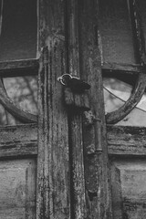 An old wooden door with peeling paint, broken glass panels, and a rusty padlock hanging at the center, creating a weathered and abandoned atmosphere.