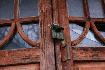 An old wooden door with peeling paint, broken glass panels, and a rusty padlock hanging at the center, creating a weathered and abandoned atmosphere.