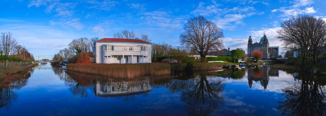 Vibrant, tranquil cityscape of Galway along the Eglington Canal with a view of Galway Cathedral, landmark buildings, and trees lining the riverbank in Ireland.